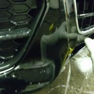 Close-up of a black car front bumper and grille with water and a yellow cable near the wheel area