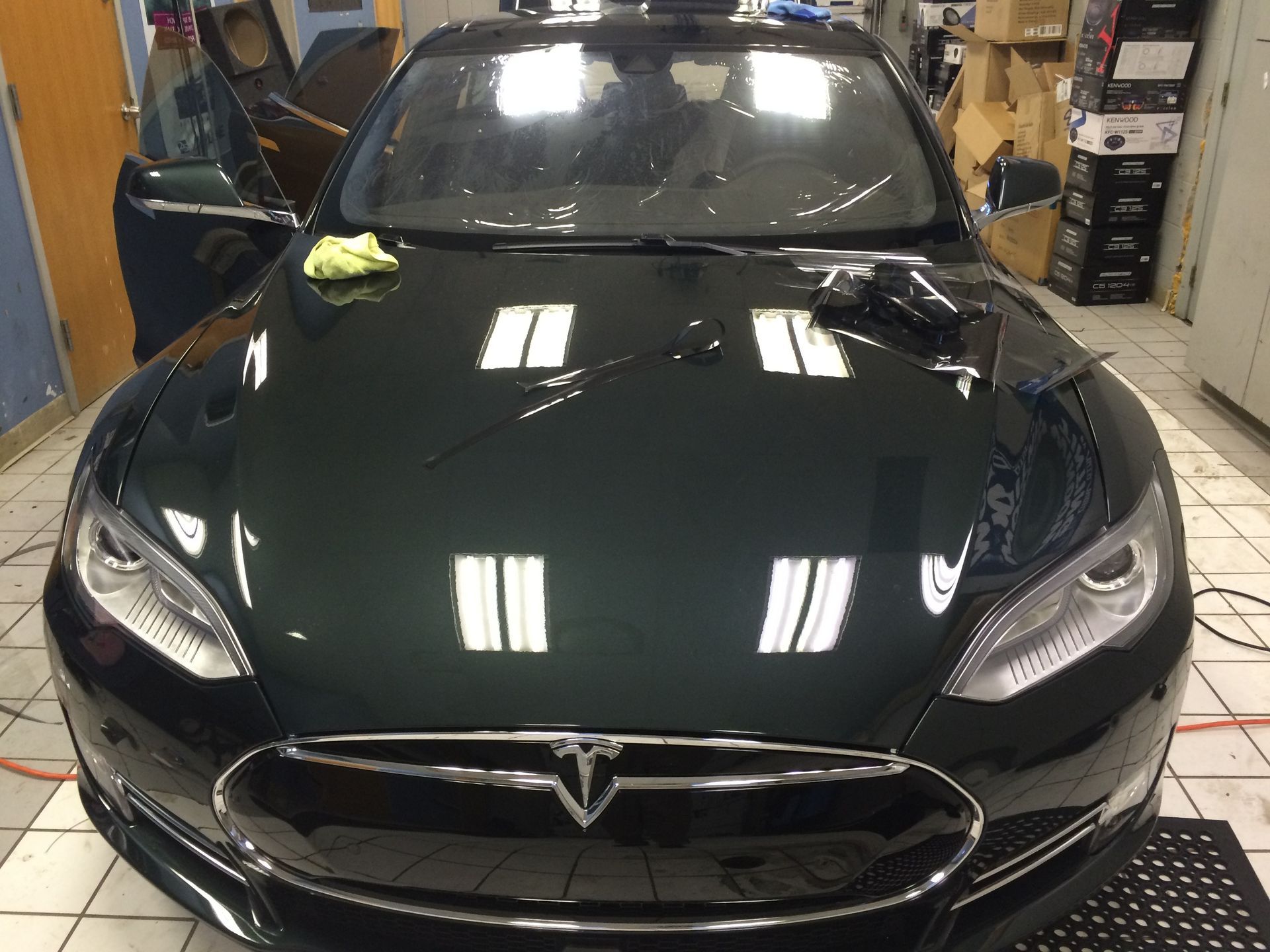 Black Tesla sedan in a showroom, front view with bright reflections on the hood.