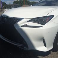 Close-up of the front of a white car with a black grille and headlight, parked outdoors.