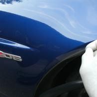 Blue car body with a hand near the wheel arch and a small badge on the side
