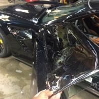 Black car with severe side damage, showing a crumpled door and damaged window frame in a garage