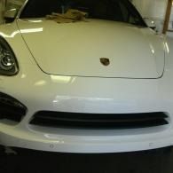 Front view of a white Porsche sports car in a garage, showing the hood and headlights.