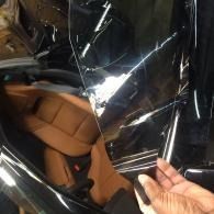 Hand holding up torn clear plastic over a tan car seat inside a vehicle