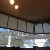 Interior view of a venue with ceiling lights and a large opening overlooking a bright structural canopy outside