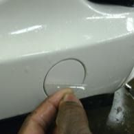 Hand peeling protective film from a white car’s fuel door area