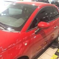 Red car parked indoors with tinted windows and a side mirror visible.