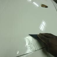 A hand wipes a white car hood with a cloth near a windshield badge.