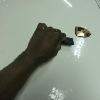 Hand holding a small black object next to a gold-colored car logo on a white glossy surface