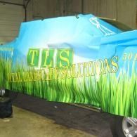Car covered with blue tarp and green grass-themed TLS Lawn Solutions wrap in a garage