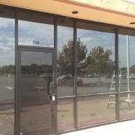 Storefront with glass windows and a door reflecting parked cars and trees outside