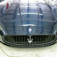 Front view of a dark blue Maserati car hood and grille with silver trident emblem.