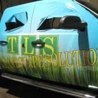 Blue car wrapped with “TLS” and “LANDSCAPESOLUTION” lettering on the side