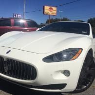 White sports car parked outdoors in a sunny lot, front view with red vehicle beside it.