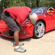Person leaning into a red sports car, inspecting the front wheel.