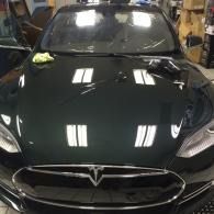 Black Tesla sedan in a garage, with a green cloth on the hood.