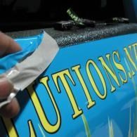 Hand placing a blue-and-yellow “CAUTIONS” sign with a silver tool