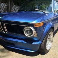 Blue classic car parked outdoors, front-left view, with chrome details and round headlights