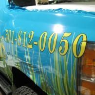 Blue vehicle side with yellow phone number and grass graphic decal