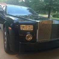 Black Rolls-Royce parked outdoors on a driveway, front view with chrome grille and headlights.