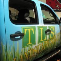Blue truck side with green-and-yellow grass logo and partial lettering.