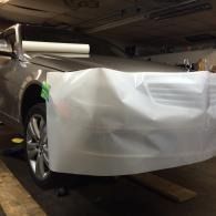 Car partially covered with a white protective sheet in a dim garage