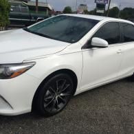 White sedan parked outdoors on wet pavement, front-left view, with dark tinted windows and black wheels