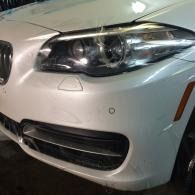 Close-up of a white BMW front bumper and headlight in a dimly lit garage