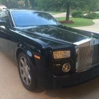 Black Rolls-Royce parked in a driveway with trees and lawn in the background