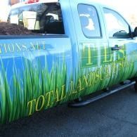 Blue pickup truck with grass-themed advertising graphics on the side, parked outdoors.