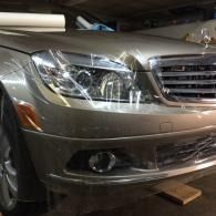 Front view of a silver car parked in a garage, with a wooden block under the bumper