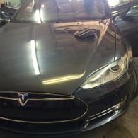 Front view of a black Tesla parked indoors with bright reflections on the hood