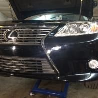 Front view of a black Lexus sedan on a blue car jack in a garage.
