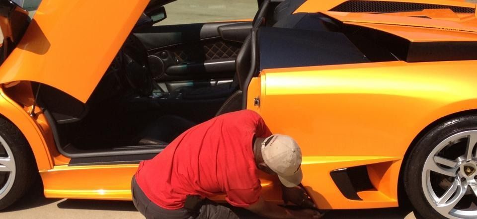 Person in red shirt working beside an orange sports car with the door open