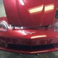 Front view of a red sports car with the hood open in a garage, showing the emblem and headlights.