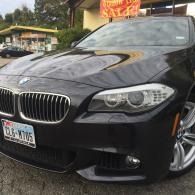 Black BMW sedan parked outdoors, front view with a visible license plate and dealership sign in the background