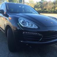 Black Porsche SUV parked outdoors on a sunny street, front-left view