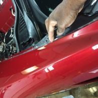 Hand adjusting a glossy red car panel near the hood