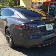 Dark gray Tesla Model Y parked on a sunny street beside a storefront
