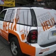 White and orange SUV with window tinting and large “HELIX” advertising decals parked by a shop