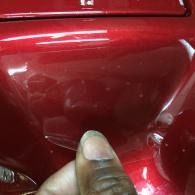 Hand holding a red glossy car panel near a dent or scratch