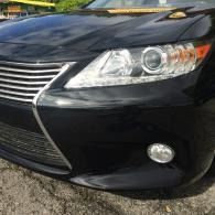 Front corner of a black sedan with chrome grille and headlight, parked outdoors on pavement