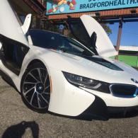 White BMW i8 with scissor doors open, parked outdoors near a stadium sign.