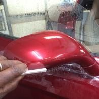 Hand holding a white tool to a glossy red car side mirror during repair