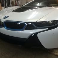 White BMW i8 sports car parked indoors, front view with blue-accented grille and butterfly door open