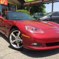 Red sports car parked under a carport on a paved driveway