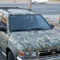 Camouflaged pickup truck parked by a road, covered in patterned wrap.