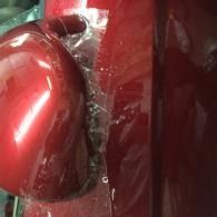 Close-up of a red car’s side mirror and glossy body panel with water droplets