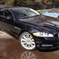 Black sedan parked on a wet driveway, with shiny alloy wheels and reflections on the ground.
