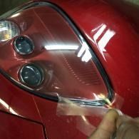 Close-up of a red car headlight as a hand peels back a clear protective film.