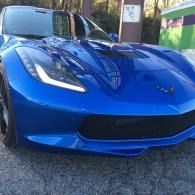 Blue sports car parked outdoors on a gravel driveway, front view.